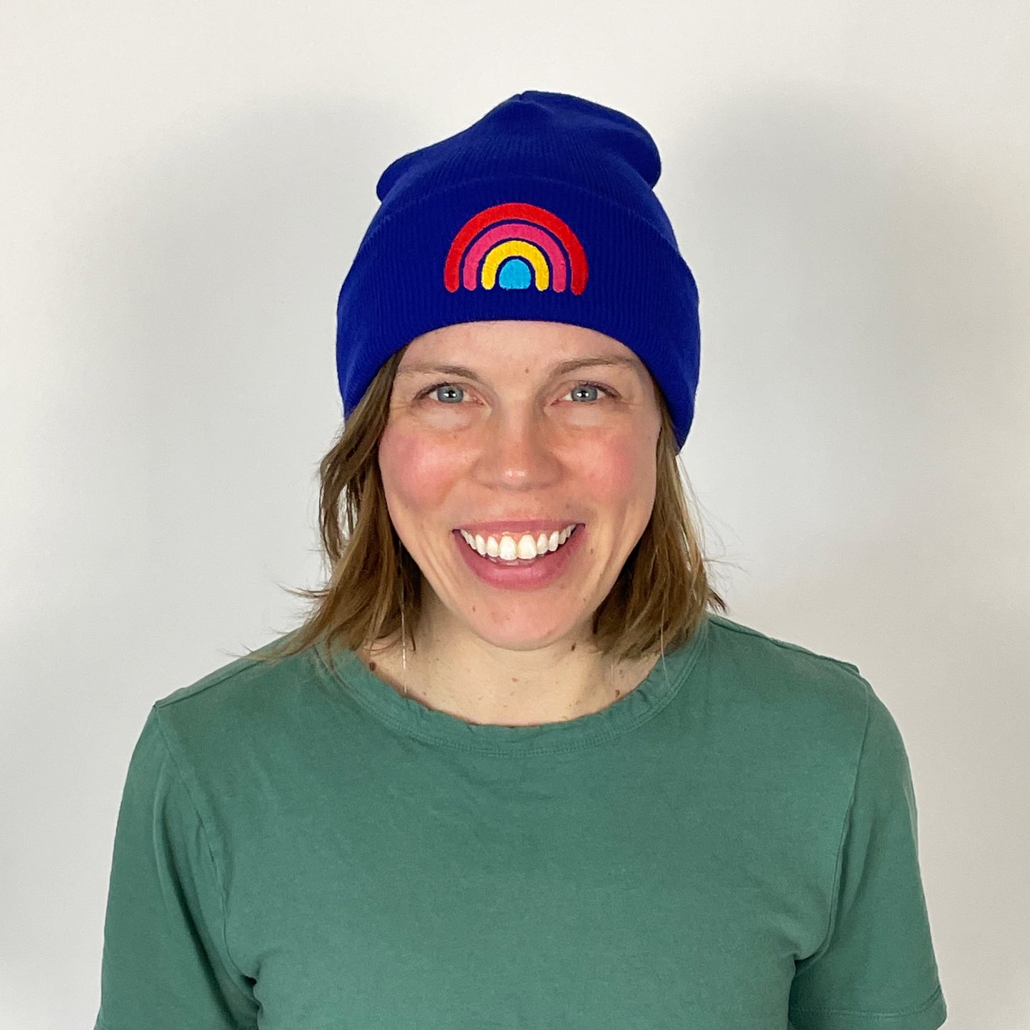 Person wearing a blue beanie with a rainbow design on a plain background